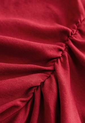 Materialul roșu prezintă o textură strânsă cu linii diagonale subtile. Țesătura pare moale și ușor elastică, evidențiind profunzimea designului.