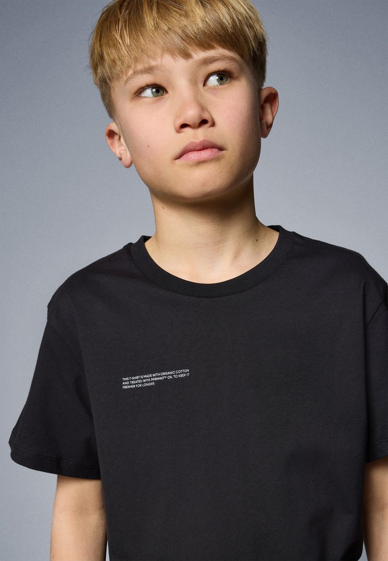 Svart t-shirt med kort ärm, tillverkad av ekologisk bomull, med liten vit text på framsidan som anger skötselråd. Enkel rund halsringning.