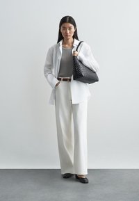 White oversized shirt, gray fitted tank, cream wide-leg pants, black woven handbag, and black flats against a light background.