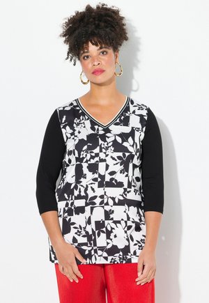 Schwarz-weißer, floral gemusterter Oberteil mit 3/4 schwarzen Ärmeln, V-Ausschnitt und einfarbigen schwarzen Abschnitten. Kombiniert mit leuchtend roten Ripp-Hosen.