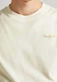 Kermana värinen puuvillapaita, jossa on pyöreä kaula-aukko ja lyhyet hihnat. Sisältää pienen, beige väriin tikatun "Pepe Jeans London" -logon.