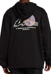 Schwarzer Kapuzenpullover mit einem Berg- und Wellenmuster in Weiß und Pastellfarben, mit dem Text "Billabong Adventure Division" auf der Mitte des Rückens.