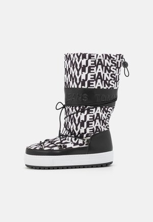Wysokie zimowe buty w czarno-białym kolorze z powtarzającym się napisem "TOMMY JEANS", czarne sznurowadła oraz gruba biała gumowa podeszwa.