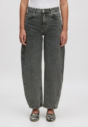 Hochtaillierte, weit geschnittene Jeans aus verblasstem grauem Denim mit einem Fünf-Taschen-Design und sichtbaren Nähten, kombiniert mit Hausschuhen im Zebramuster.