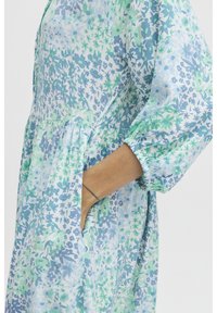 Vestido con estampado floral en azul claro y verde. Presenta un corte relajado, mangas elásticas y bolsillos laterales para mayor funcionalidad.
