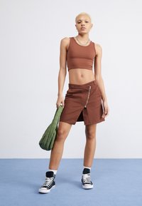 Top corto marrón, falda mini marrón con cremallera al frente, bolso verde con hombros abullonados, zapatillas altas negras, calcetines blancos de tipo crew, texturas suaves.