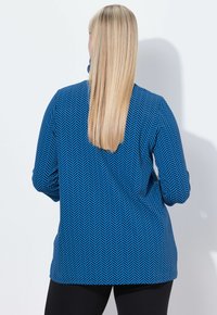 Top de manga larga azul con un patrón de espiga, que presenta un corte relajado y un dobladillo redondeado, fabricado con una tela ligera y texturizada.