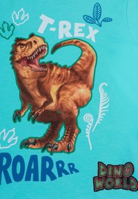 T-shirt turchese con un grande grafico colorato di un T-Rex, con il testo "T-REX" e "ROARRR" in grassetto. Gli accenti includono design di foglie e impronte.