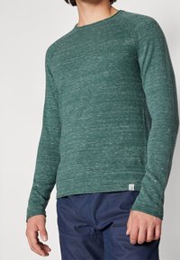 Långärmad grön tröja i jersey med strukturerad väv, med rund halsringning och en liten logotypetikett i fållen.