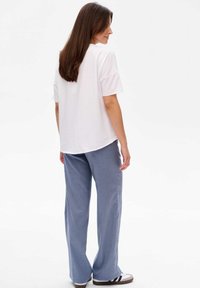 Weißes T-Shirt mit kurzen Ärmeln kombiniert mit hellblauen, weiten Hosen, die eine glatte Textur und ein dezentes Saumdetail aufweisen.