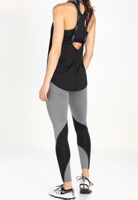 Nainen, joka on pukeutunut mustaan urheilulliseen tanktoppiin, jossa on Nike-hihnat, harmaisiin ja mustiin legginsseihin sekä valkoisiin Nike-lenkkareihin, seisoo selkä kameraan päin.