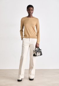 Beżowy sweter z długim rękawem, kremowe spodnie o szerokich nogawkach oraz czarna torebka w kwiatowy wzór. Grube białe buty na platformie. Prosty design.