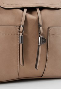 Beige läderväska med en slät yta, med lockstängning, två parallella banden och metallisk hårdvara.