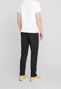 Smal passform svarta byxor med vertikala vita ränder, tillverkade av mjukt tyg. I kombination med en enkel vit T-shirt och beige sneakers.