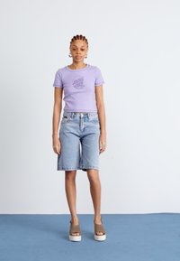 Purple short-sleeve t-shirt with “Santa Cruz” graphic, paired with light denim bermuda shorts and taupe platform sandals. Simple, casual ensemble.