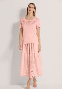 Rosa Kurzarm-Oberteil mit dekorativen Ausschnitten am Ausschnitt, kombiniert mit einem langen, passenden rosa Rock mit kreisförmigen Ausschnittmustern.