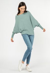 Lichtblauwe oversized trui met brede mouwen, gecombineerd met aansluitende lichtblauwe jeans en witte sneakers. Eenvoudig ontwerp, zachte textuur.