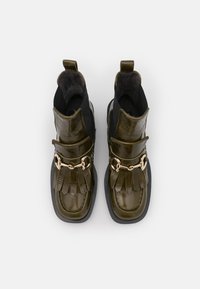 Pair of shiny dark olive green ankle boots with fringe and gold metal bit detail, square toes, and black elastic side panels.