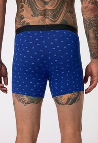 Blaue Boxershorts mit einem schwarzen Bund, verziert mit einem kleinen weißen Blumenmuster. Der Stoff wirkt weich und hat einen engen Sitz.