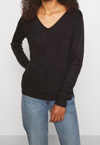 Svart v-ringad tröja i mjukt stickat material, med långa ärmar, smal passform och ribbade ärmslut och nederkant. Bärs tillsammans med blå jeans.