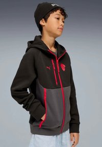 Zwarte en grijze hoodie met rits en rode accenten, met een logo, voorzakken en een capuchon. Gemaakt van een zachte stof.