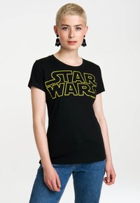 Black t-shirt featuring a large yellow "STAR WARS" logo on the front. Short sleeves with a round neckline, made of soft cotton fabric.