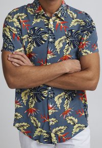 Korte mouwen overhemd met knopen in het blauw, met een tropisch blad- en bloemenpatroon in geel en rood. De stof is soepel en heeft een relaxte pasvorm.