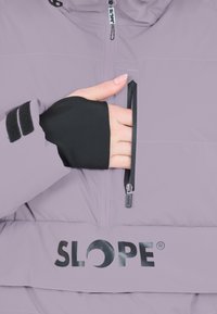 Lyslilla jakke med høj krave, der har en lynlåslomme på brystet og sorte detaljer på manchetterne. Viser "SLOPE" logoet på forsiden.