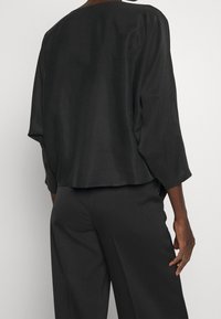 Haut noir ample avec un col large, des manches trois-quarts et une texture lisse. Associe à un pantalon large foncé assorti.