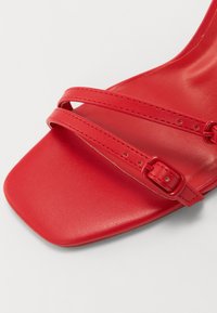 Sandale en cuir rouge avec deux fines sangles croisées munies d'une boucle, un bout carré, et une semelle lisse.
