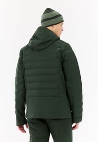 Žalios spalvos izoliuota striukė su kapišonu, su antklodine apdaila, lygiu paviršiumi ir logotipu viršuje ant nugaros. Derinama su raiškia kepure.