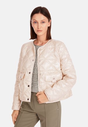 Gep quiltete, cremefarbene Jacke mit rundem Halsausschnitt, Druckknöpfen, Taschen vorne und glänzender Textur. Sie wird über einem leichten Pullover getragen.