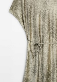 Robe en tissu léger et frais de couleur crème avec un motif texturé et marbré. Présente une coupe fluide et une ceinture à nouer à la taille.