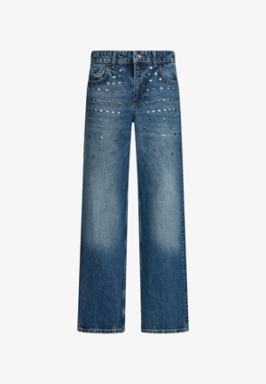 Vaqueros azules de corte recto con efecto desgastado y tachuelas plateadas dispuestas en un patrón degradado cerca de los bolsillos delanteros y los muslos superiores.