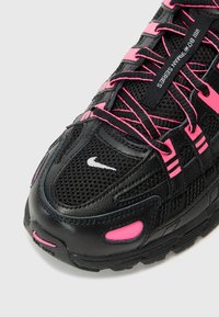 Schwarzer Sportschuh mit einem strukturierten Mesh- und Lederobermaterial, mit pinken Akzenten und Schnürsenkeln. Beinhaltet ein weißes Logo in der Nähe der Zehen.