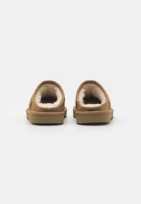 Scarpe marroni slip-on con una morbida fodera interna bianca, esterno testurizzato e suola piatta in gomma bassa. Presentano un tallone arrotondato e bordi lisci.