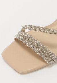 Sandal con tacco beige caratterizzato da tre fasce di strass luccicanti, design con punta quadrata e una soletta liscia e opaca.