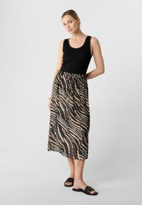 Schwarzes Tanktop kombiniert mit einem langen, fließenden Rock im beige-schwarzen Tigerstreifenmuster. Die Accessoires umfassen schwarze Slidesandalen.