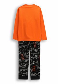 Pomarańczowa koszula z długim rękawem połączona z czarnymi spodniami, na których znajdują się białe i czerwone napisy oraz grafiki skateboardów, wyeksponowana na białym tle.