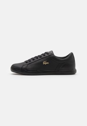 Schwarzer Low-Top-Ledersneaker mit Schnürung vorne und goldenem Krokodillogo an der Außenseite, flacher Sohle und strukturiertem Fersendetail.