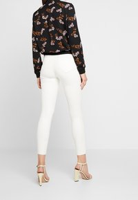 Svart blommig långärmad blus med rosa och bruna blommönster. Matchas med figurnära vita jeans och beiga klacksandaler.