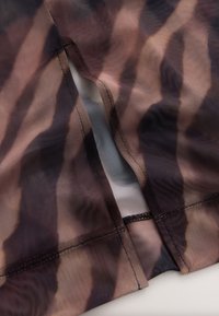 Tessuto di rete trasparente con un motivo a strisce ondulate marroni e nere. Presenta una cucitura con filo nero e uno strato interno bianco leggermente opaco.