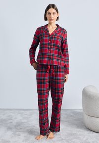 Rød rutete pysjamas-sett med en knapp-opptopp med krage og lange ermer, samt matchende bukser med snor, laget av myk stoff.