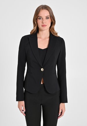 Zwarte op maat gemaakte blazer met een notch lapel, enkele gouden knoopsluiting en een slanke silhouet. Draagt over een zwarte top, gecombineerd met bijpassende broek.