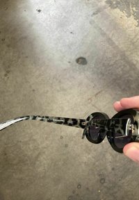 Sorte cat-eye solbriller med et gennemsigtigt hornmønster, runde linser og en tynd stang med brandindgravering. Glat tekstur overalt.