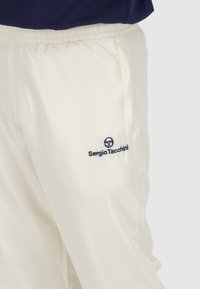 Witte, lichte stoffen broek met een elastische tailleband. Heeft een marineblauw logo aan de linkerkant, dat een strakke, minimalistische stijl benadrukt.
