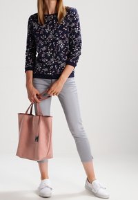 Marineblauwe trui met bloemenpatroon, lichtgrijze cropped jeans en een roze tote bag. Witte instappers met een riempje maken de look compleet.