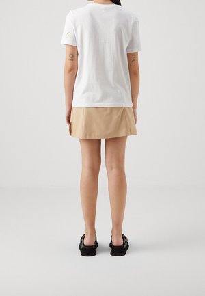 White short-sleeve T-shirt with a lemon graphic on the left sleeve, paired with a beige pleated mini skirt and black shoes.