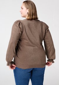 Bruine metallic gebreide trui met pofmouwen en gerimpelde manchetten; gecombineerd met blauwe spijkerbroeken. De trui heeft een zachte textuur en een ontspannen pasvorm.