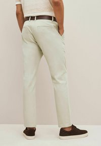 Chinos vert clair, ajustés, avec deux poches arrière, associés à des chaussures en suède marron foncé. Le tissu semble lisse avec une finition soignée.